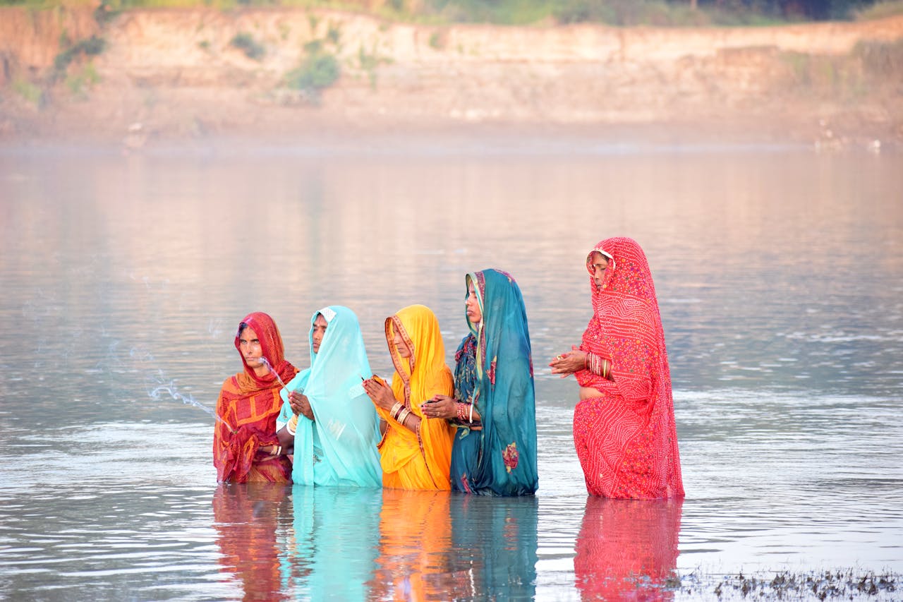 Women in vibrant saris performing Chhath Puja in a serene river environment.