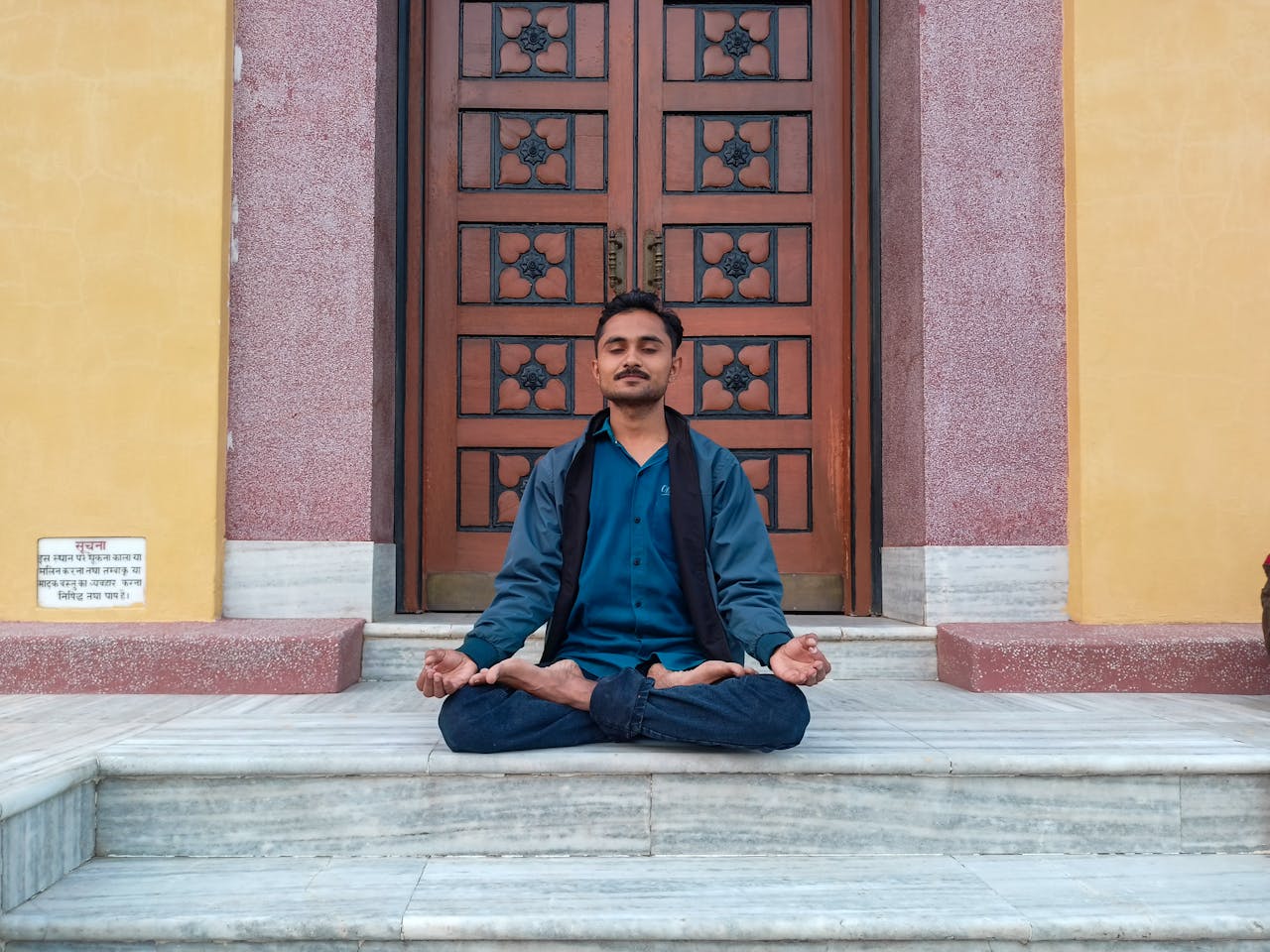 Man in meditation pose at a monastery entrance, embodying tranquility and mindfulness.