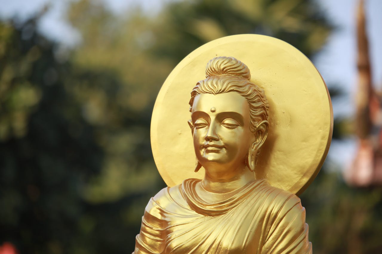 Close-up of a golden Buddha statue with a serene expression, sunlit with a blurred background.